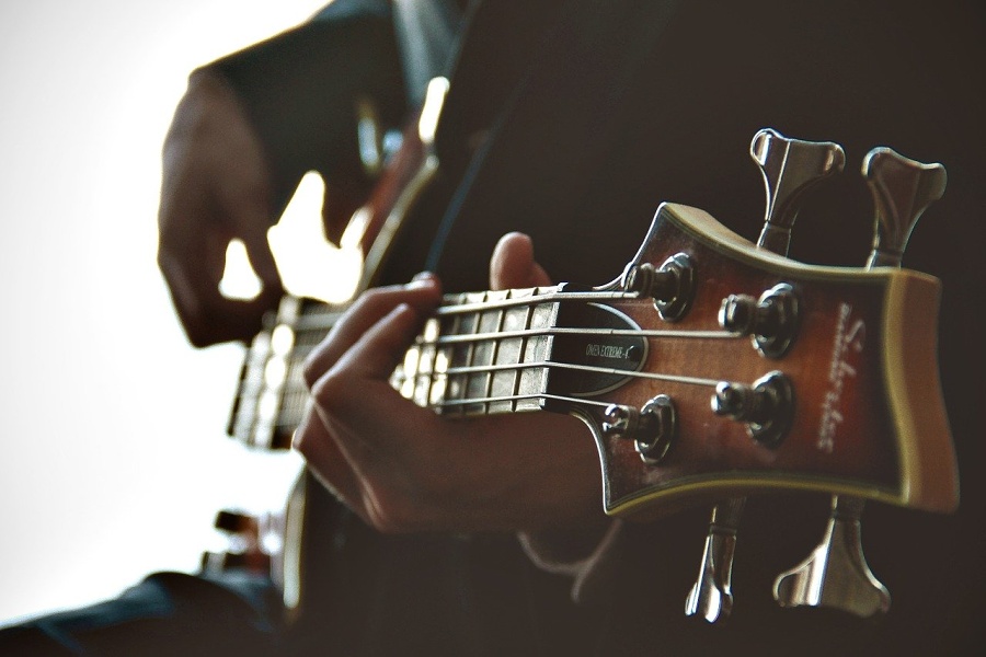 Na zdjęciu widać gitarzystę, który gra na gitarze basowej.