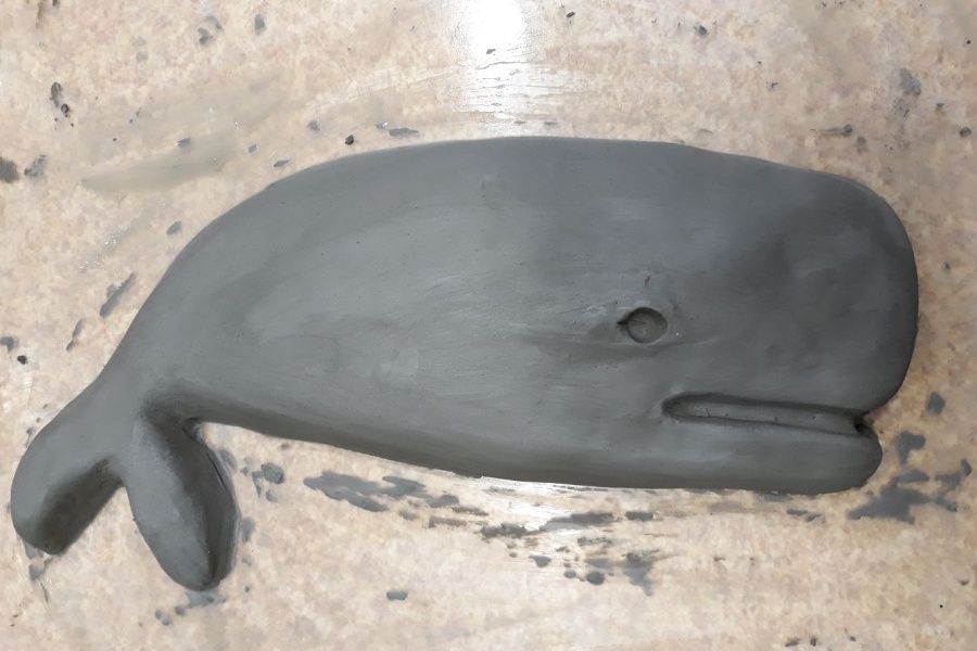 Gliniana płaskorzeźba w kształcie wieloryba leżąca na gładkiej powierzchni