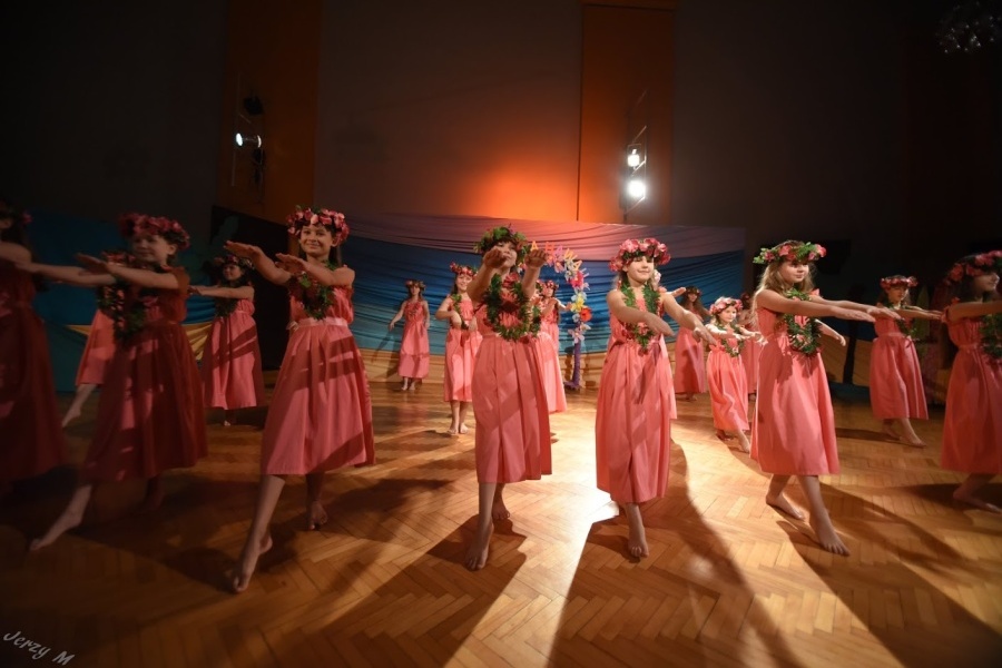 Grupa dziewcząt w różowych sukniach i wiankach na głowach stoi w tanecznej pozie