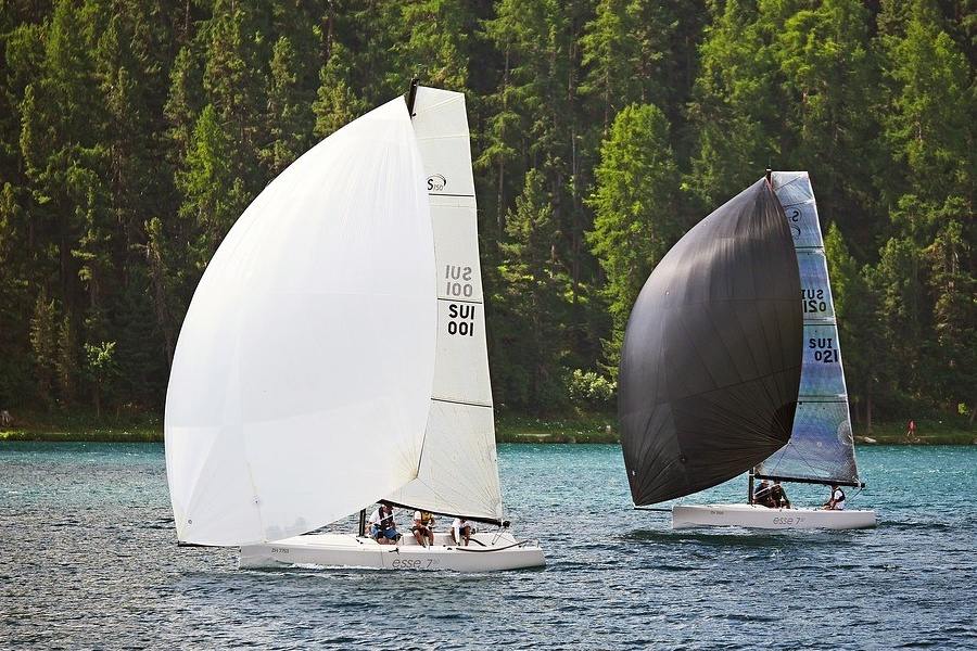 Dwa jachty pod pełnymi żaglami ścigają się na wodach jeziora na tle zalesionego brzegu