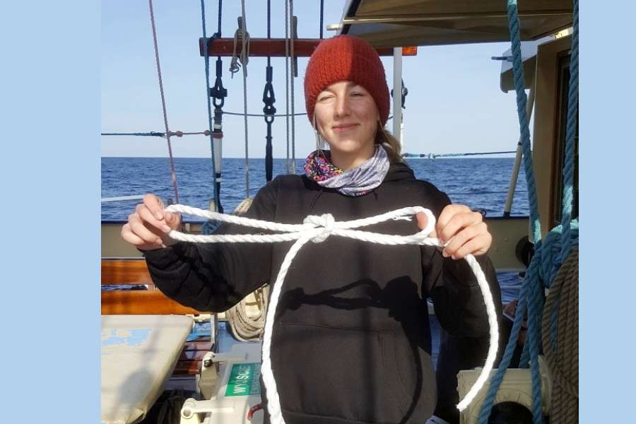 Na pokładzie żaglowca STS KAPITAN BORCHARDT uczennica Karolina trzyma przed sobą białą linkę z zawiązanym węzłem. Za plecami widać spokojne morze.