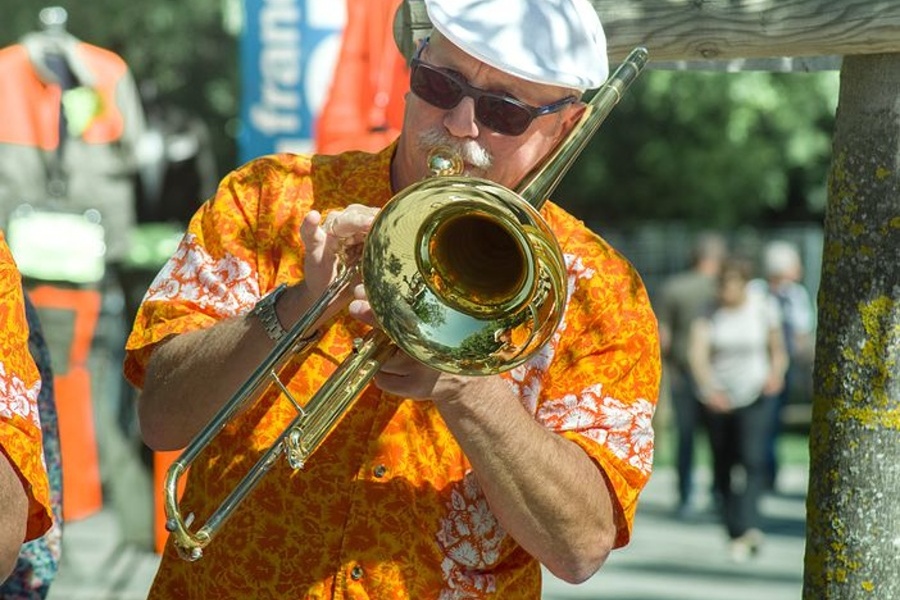 Na zdjęciu widać mężczyznę w kolorowej koszuli i białym kapeluszu, który gra na puzonie.