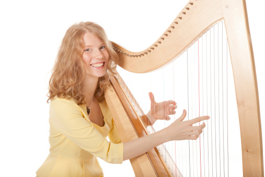 Na zdjęciu widać młodą uśmiechniętą kobietę,która gra na harfie