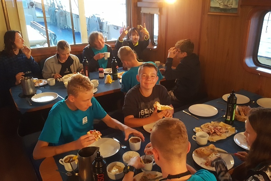 Mesa, grupa żeglarzy sześć osób spożywa posiłek przy stole zastawionym jedzeniem.