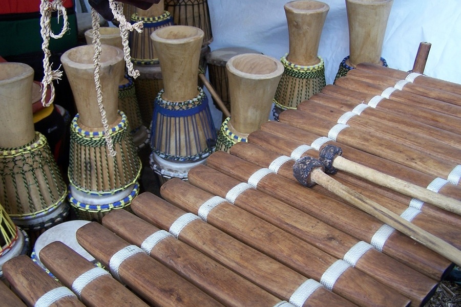 Zdjęcie przedstawia afrykański instrument zwany balafonem oraz odwrócone do góry nogami kilka afrykańskich bębnów pod nazwą djembe