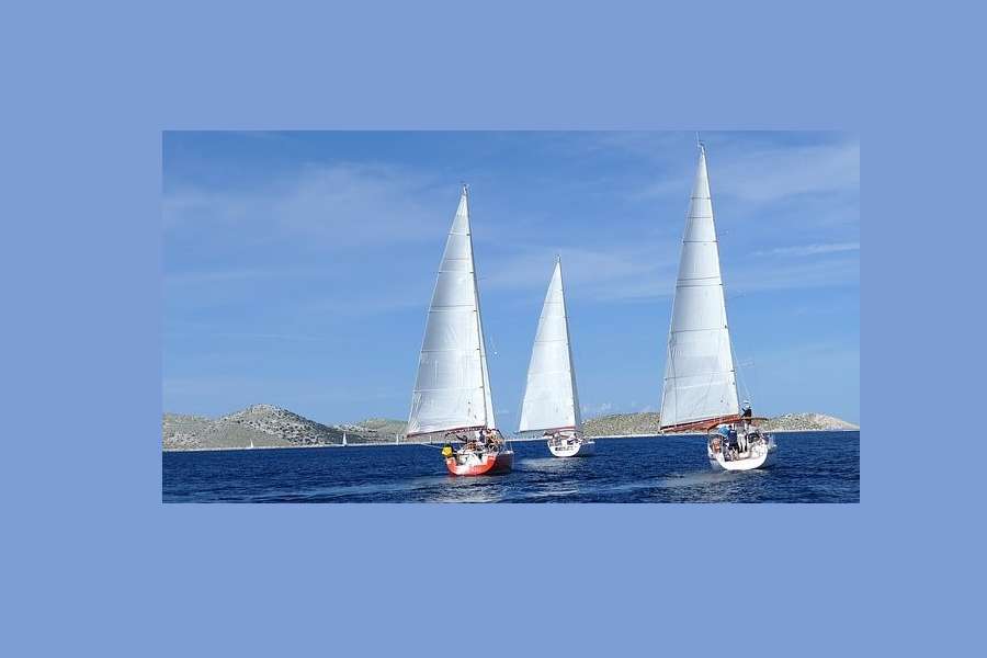Trzy jachty płyną pełnym kursem po morzu na horyzoncie widoczne pagórkowate wyspy