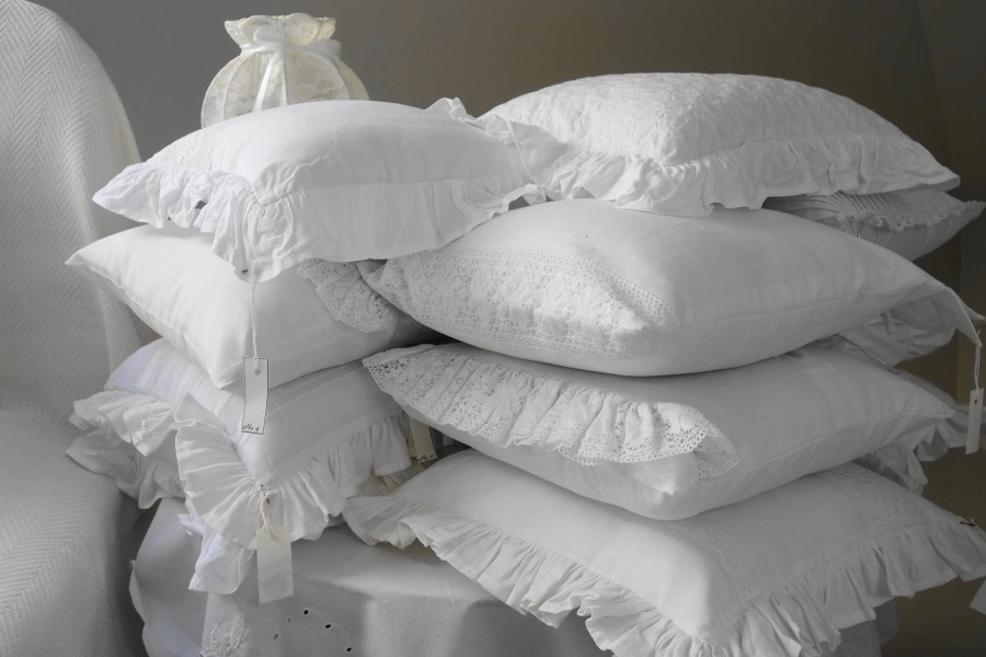 Zdjęcie przedstawia dwie sterty białych, koronkowych poduszek