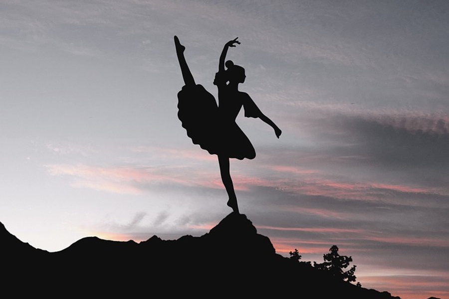 Zdjęcie przedstawia tancerkę stojąca na skale z nogą i ręką  uniesiona do góry