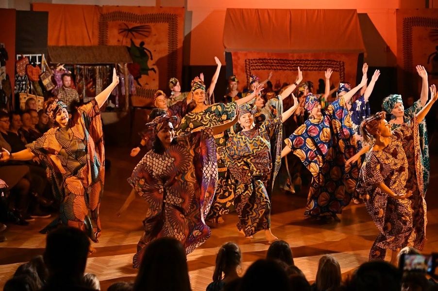Grupa kobiet w kolorowych sukniach z motywami afrykańskimi, z turbanami na głowach, w tanecznej pozie z rękami do boku.