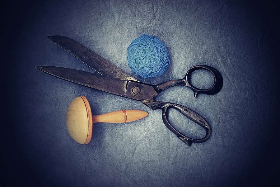 Zdjęcie przedstawia stare nożyczki, drewniany naparstek i niebieski kłębek nici.