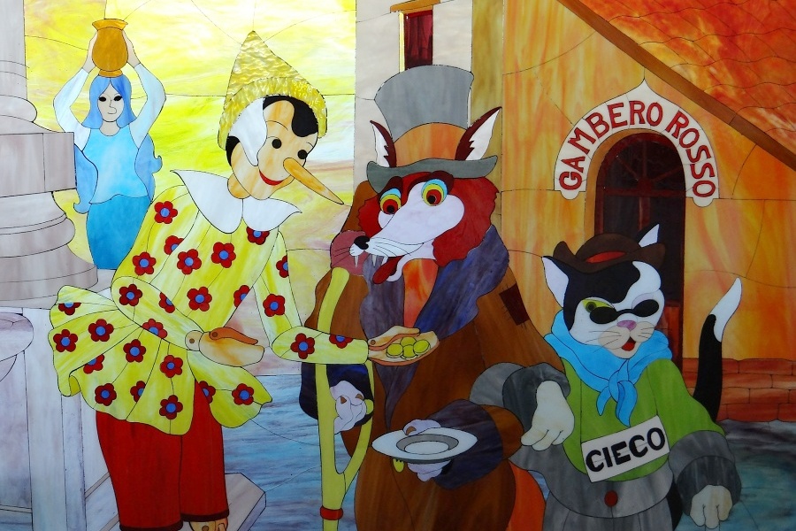 Zdjęcie przedstawia kolorowy rysunek, który przedstawia Pinokia, Lisa i Kota.