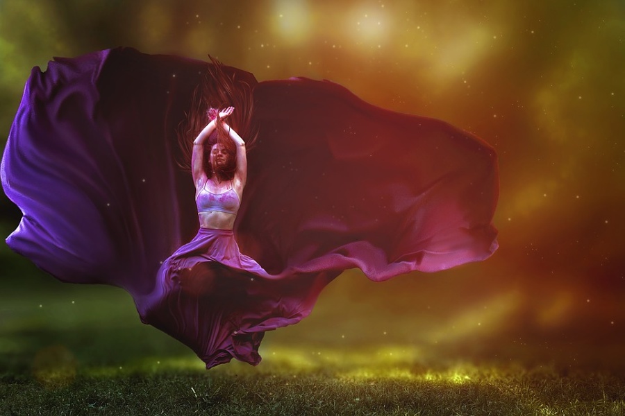 Zdjęcie przedstawia postać tancerki w zwiewnej długiej fioletowej spódnicy unoszącej się nad głową.