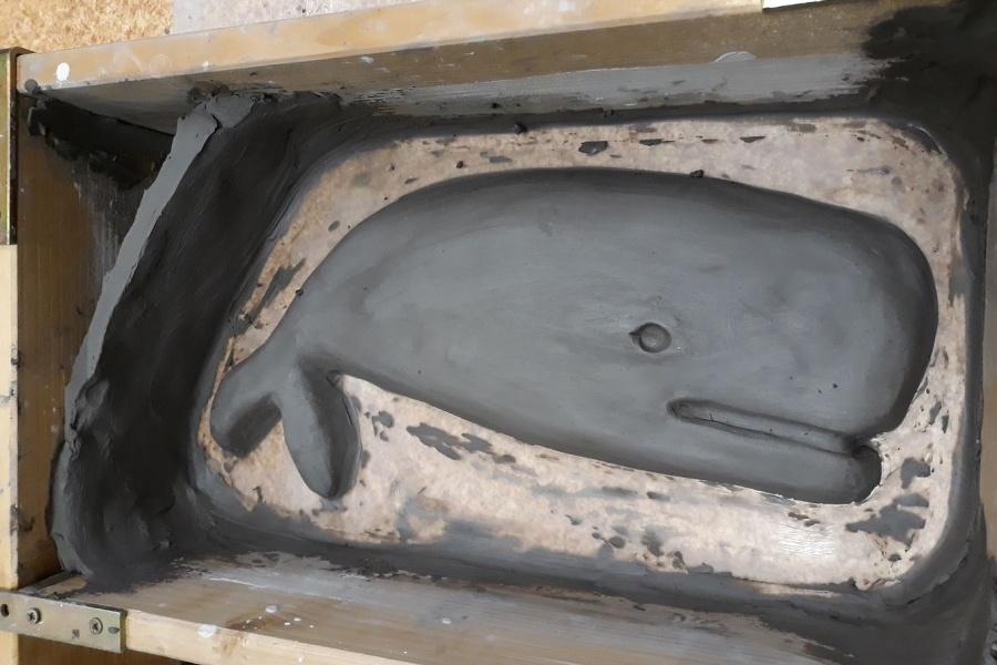 Gliniana płaskorzeźba w kształcie wieloryba leżąca w skrzynce