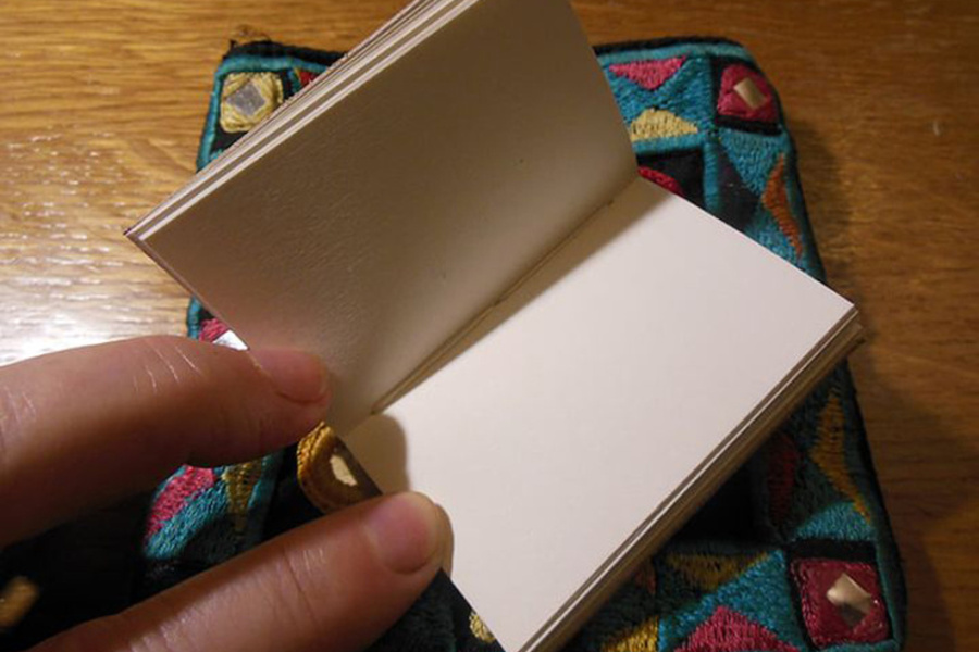 dłoń trzymająca mały notesik z białymi kartkami