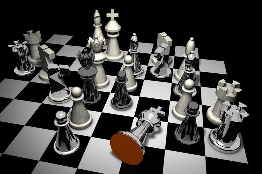 Błyszczące białe i czarne figury na szachownicy, z przewróconym czarnym królem