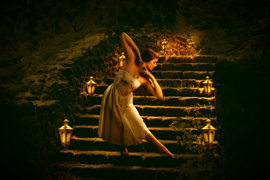 tancerka stojąca na schodach, po obu stronach zapalone lampy
