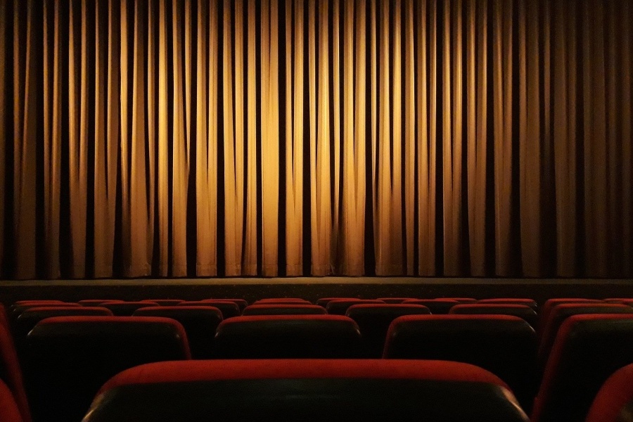 Widownia teatralna z widocznymi czerwonymi krzesłami i jasnobrązową kurtyną spuszczoną na scenę