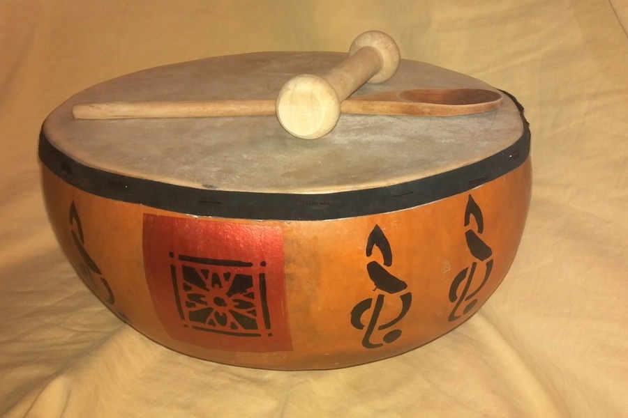 Zdjęcie przedstawia etniczny instrument perkusyjny a na nim położone drewniana łyżka oraz tłuczek