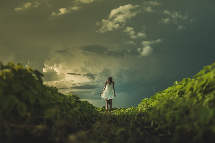 Zdjęcie przedstawia kobietę stojącą na zielonej trawie, na tle nieba.