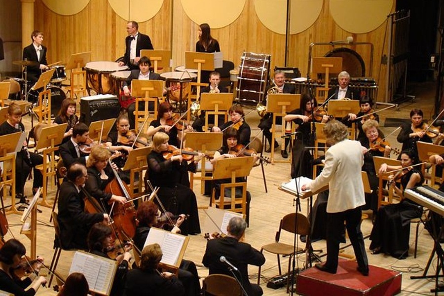 Na zdjęciu widać orkiestrę symfoniczną i dyrygenta za pulpitem dyrygenckim.