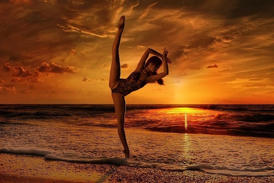 Zdjęcie przedstawia ćwiczącą dziewczynę na plaży przy zachodzie słońca