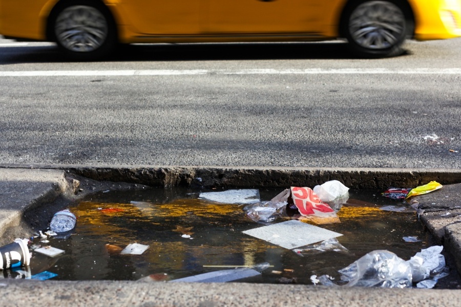 Zdjęcie przedstawia ulicę, na której leżą rozsypane śmieci w kałuży wody.