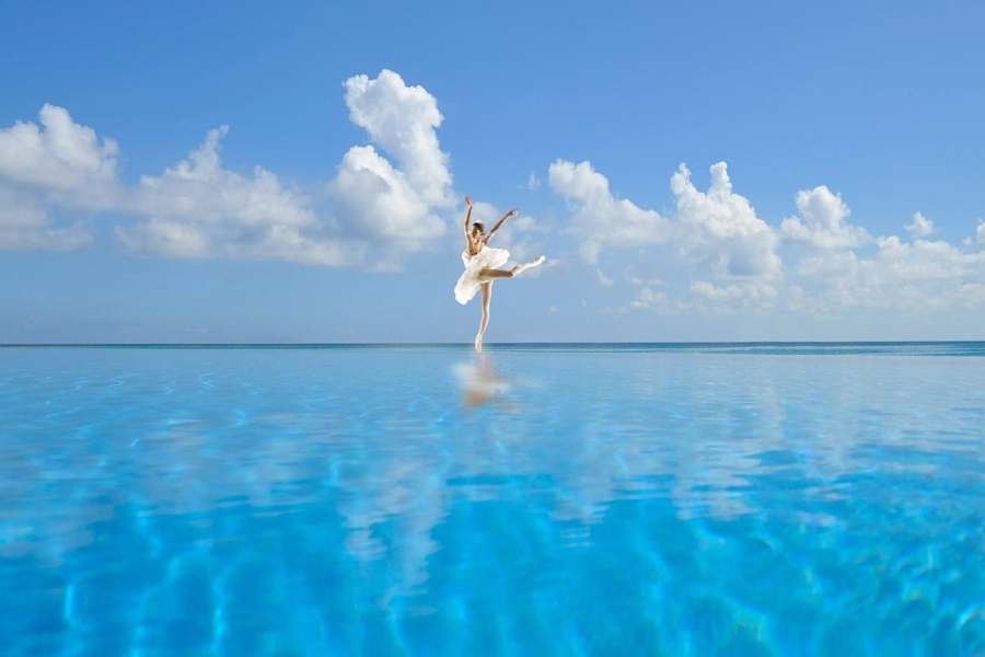 Zdjęcie przedstawia baletnicę stojącą na pointach w środku oceanu w pozycji arabesque.