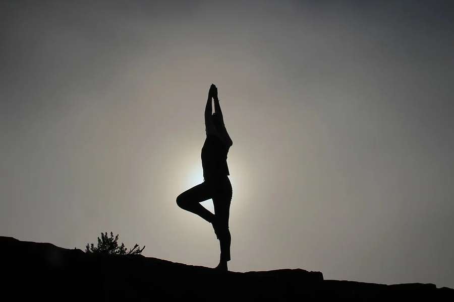 Zdjęcie przedstawia sylwetkę osoby praktykującej jogę o zachodzie słońca.