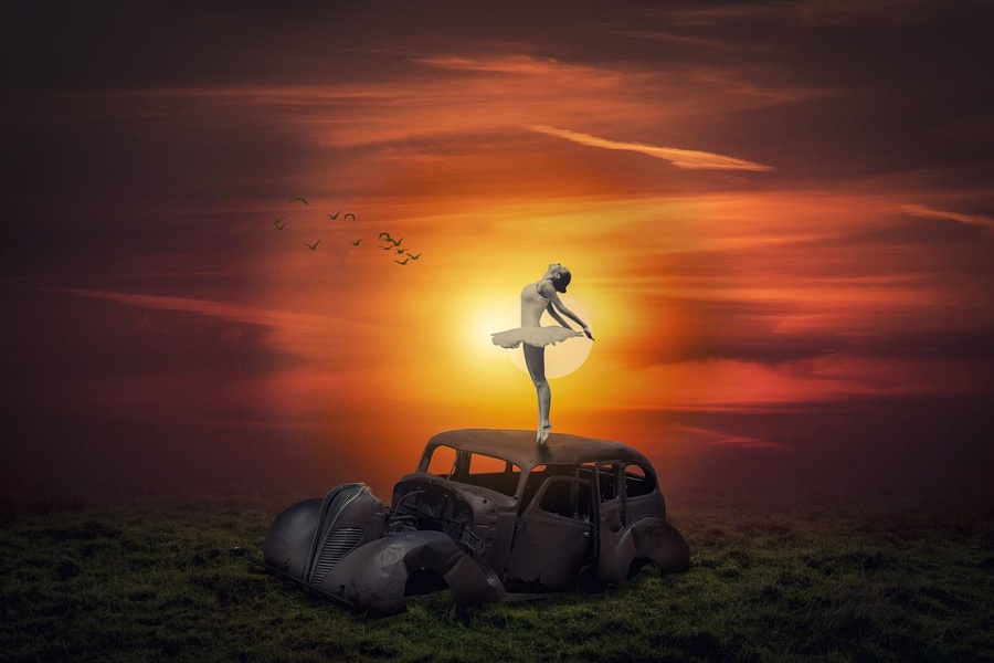 Zdjęcie przedstawia baletnicę stojącą na wraku samochodu przy zachodzie słońca.